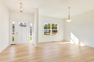 Bright empty room in Poplar Village with light wood floors, white walls, large window, and glass front door.