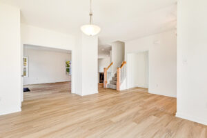 Bright, empty room in Poplar Village Lot 23 with light wood floors, white walls, and a wooden handrail staircase.