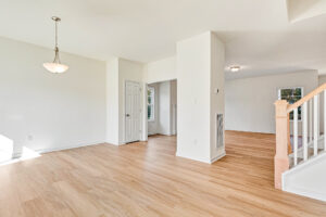 Bright, empty living space in Poplar Village’s Lot 23 with light wood floors, white walls, and a staircase.