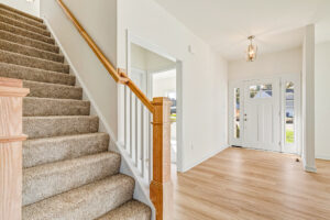 Bright entryway at Lot 23, Poplar Village, featuring wooden stairs, white walls, and a door with glass windows.