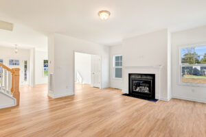 Bright, empty living room in Poplar Village Lot 23 with light wood floors, white walls, fireplace, and large windows.