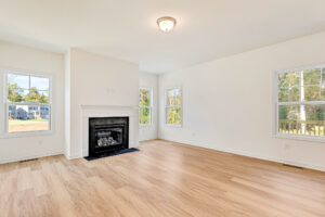 Bright, empty living room in Poplar Village Lot 23 with light wood floors, white walls, fireplace, and large windows.