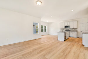 Bright open-concept living in Poplar Village Lot 23 with light wood floors and a modern white kitchen.