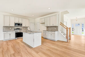 Modern kitchen with white cabinets, granite island, and wood floors in Poplar Village's Lot 23, near entryway and stairs.