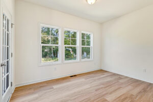 Bright, empty room in Poplar Village's Lot 23 with three large windows, light wood flooring, and off-white walls.