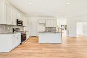 Modern kitchen in Poplar Village with white cabinets, stainless steel appliances, island, and light wood flooring.