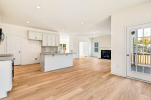 Modern kitchen and living area in Poplar Village’s Lot 23 with light wood floors, white cabinets, and patio access.