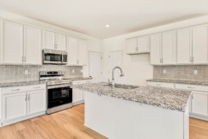 Modern kitchen in Poplar Village with white cabinets, granite countertops, and a central island sink.