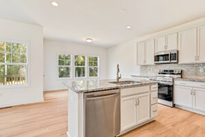 Bright modern kitchen in Poplar Village with white cabinets, granite island, and stainless steel appliances.