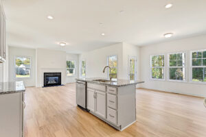Bright, modern kitchen with island, wood floors, and large windows in Poplar Village Lot 23, open to living area with fireplace.