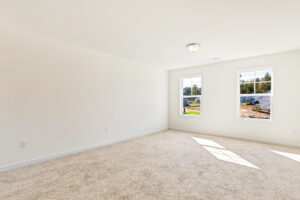Empty, carpeted room with white walls in Poplar Village, ceiling light, and two windows letting in natural light.