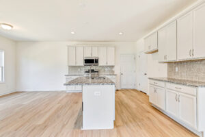 Modern kitchen in Poplar Village with white cabinets, granite countertops, island, and light wood flooring.