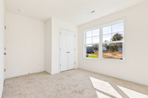 Bright, empty bedroom in Lot 23, Poplar Village with beige carpet, white walls, closet, and large sunny window.
