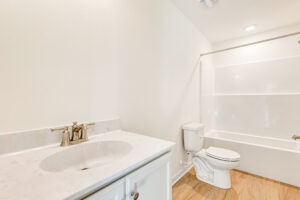 Bright, clean bathroom in Poplar Village features a white vanity, sink, toilet, and bathtub with shower curtain rod.