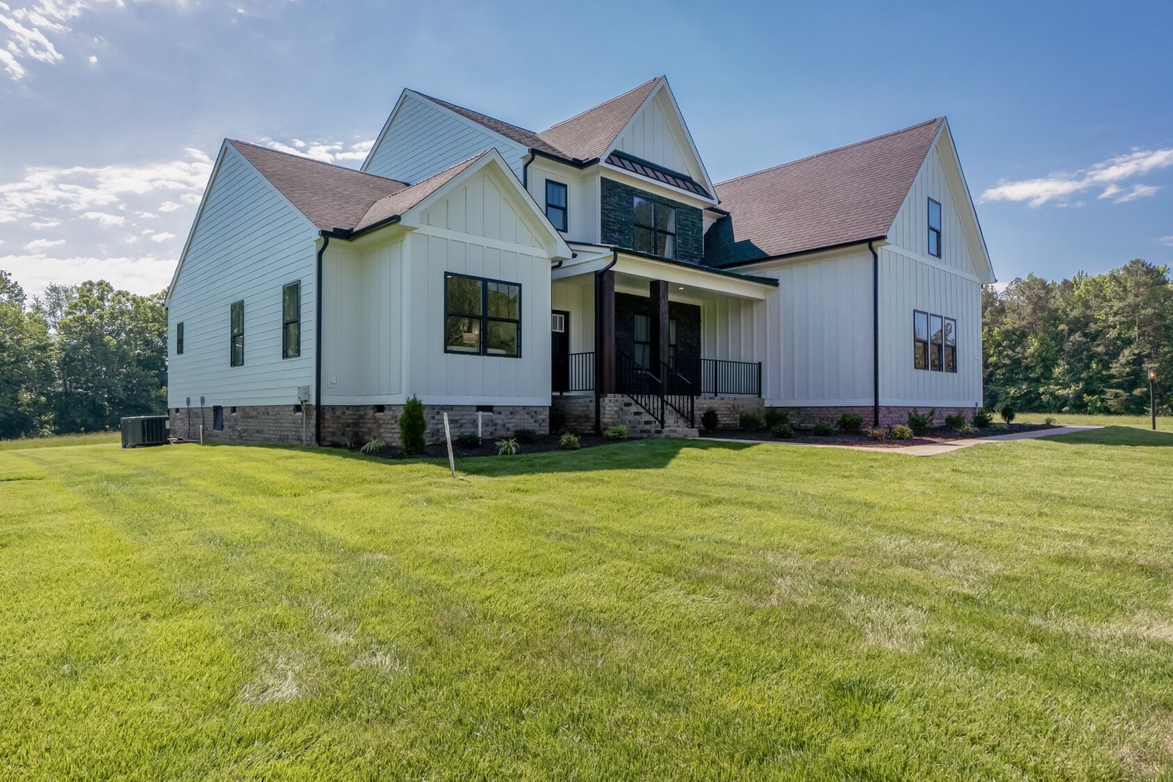 Modern white house with dark trim in Hanover’s Shirley Commons, large windows, and a spacious green lawn on a sunny day.