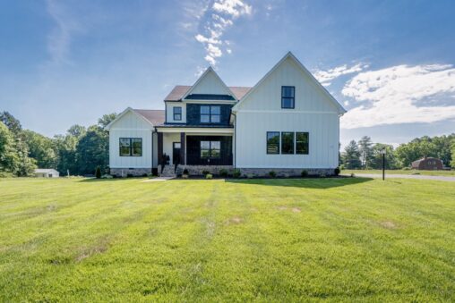 Modern Hanover white farmhouse with black trim on a large, green lawn under a blue sky with scattered clouds.