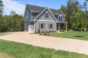 Blue two-story house with white trim in Poplar Village, Lot 13, featuring a porch, driveway, and green lawn.