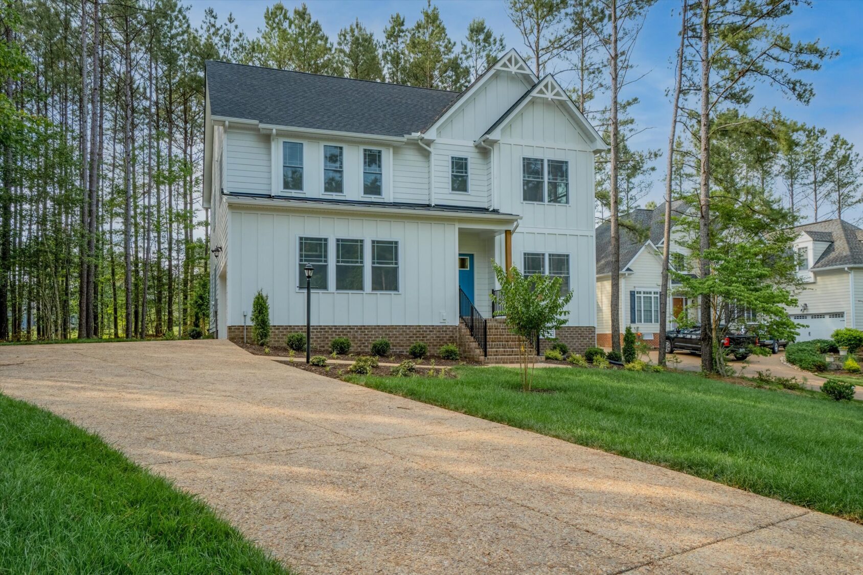 Two-story white house in Poplar Village with a sloped driveway, green lawn, and surrounded by tall trees.