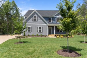 Two-story gray house with white trim on Lot 13 in Poplar Village; front porch, green lawn, and wooded background.