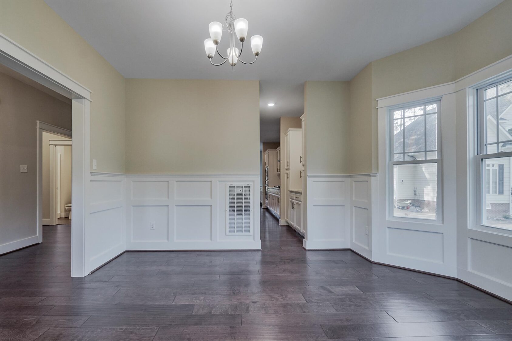 Empty Albany dining room with dark wood floors, white wainscoting, chandelier, and large windows.