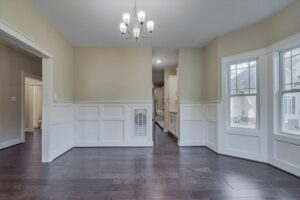 Empty Albany dining room with dark wood floors, white wainscoting, chandelier, and large windows.