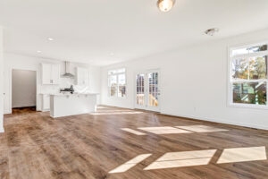 Bright, empty open-plan kitchen and living area in Poplar Village Lot 13 with wood floors and large windows.