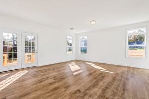Bright, empty room with wood floors in Poplar Village, Lot 13; large windows and double doors open to a small porch.