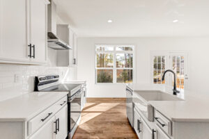 Bright modern kitchen in Poplar Village’s Lot 13 with white cabinets, island sink, and sunlit stainless appliances.