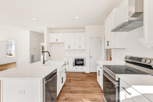 Modern white kitchen with stainless steel appliances and island in bright Poplar Village Lot 13 open space.
