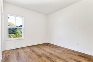 Bright empty room with wood-style floors at Lot 13, Poplar Village, featuring white walls and natural light.