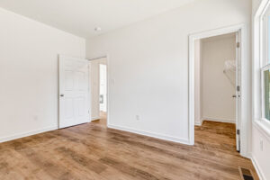 Bright, empty room in Poplar Village’s Lot 13 with wood floors, white walls, and a large window for natural light.