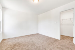 Empty room in Poplar Village, Lot 13, with beige carpet, white walls, window, and open closet with wire shelving.