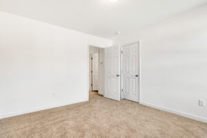 Empty room in Poplar Village, featuring beige carpet, white walls, and two open doors leading to a hallway.