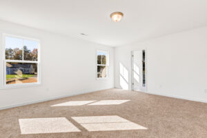 Bright, empty room in Poplar Village with beige carpet, white walls, two windows, and a ceiling light fixture.