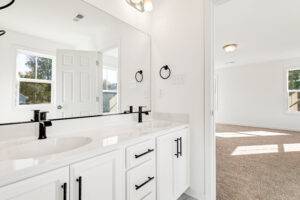 Bright bathroom in Poplar Village with double sinks, black fixtures, white cabinets, and a view into a sunlit room.