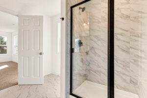 Bright bathroom in Lot 13, Poplar Village, with marble tile and glass shower, opens to a carpeted room.