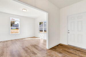 Bright, empty room with wood floors in Poplar Village, Lot 13. White walls and large windows let in natural light.
