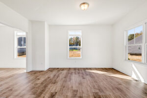 Bright empty room in Poplar Village with wood flooring, white walls, and large windows letting in natural light.