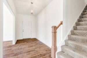 Bright entryway in Poplar Village Lot 13 with wood floors, white walls, carpeted stairs, and a white front door.