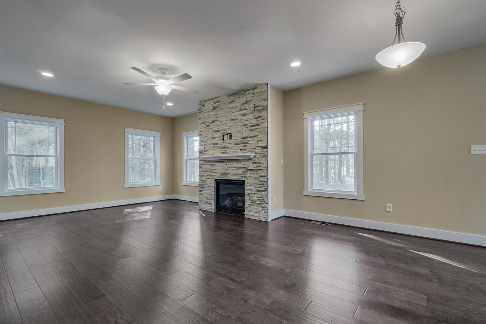 Spacious living room in Poplar Village with dark hardwood floors, stone fireplace, beige walls, and large windows.