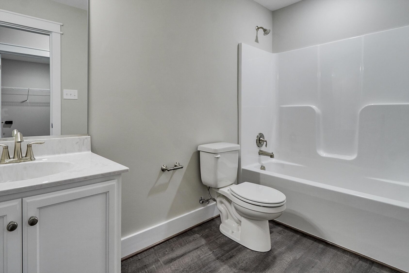 Modern Poplar Village bathroom with white vanity, toilet, tub, and gray wood-look flooring in Albany.