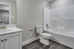 Modern Poplar Village bathroom with white vanity, toilet, tub, and gray wood-look flooring in Albany.