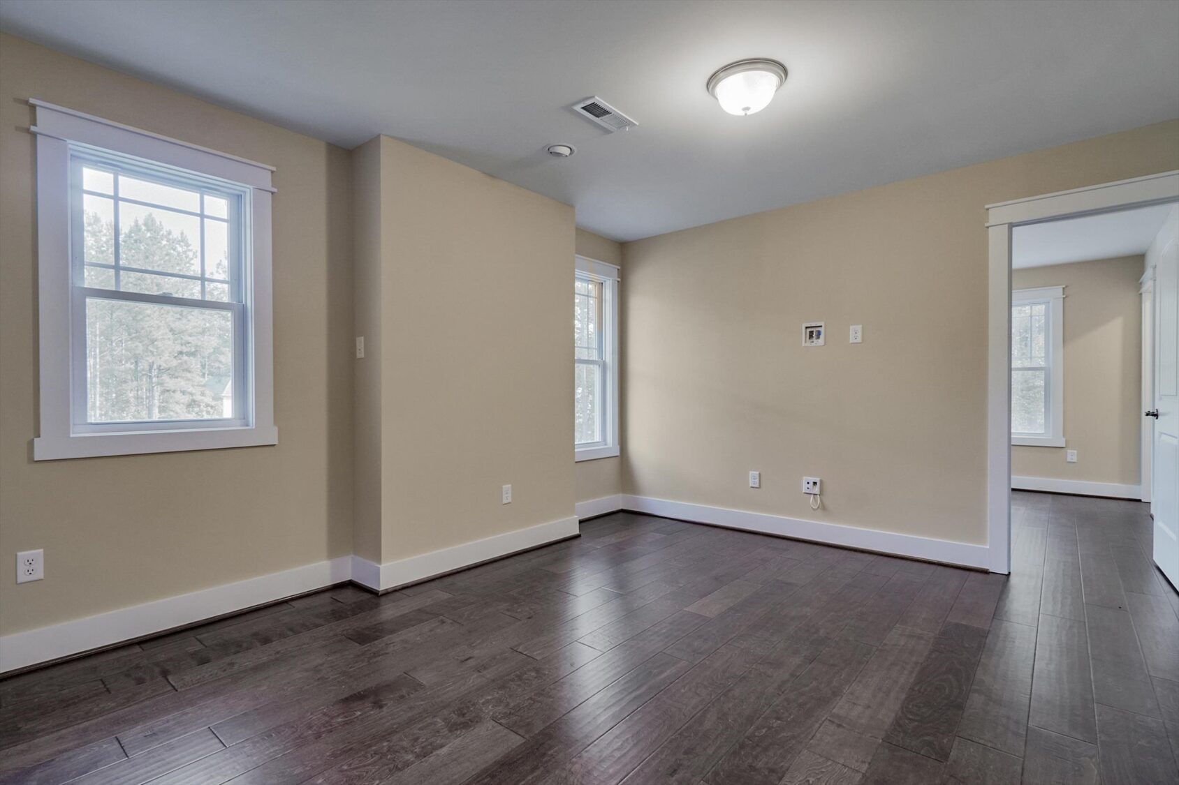 Empty room in Poplar Village, Albany with beige walls, dark wood floor, white trim, and natural light from many windows.