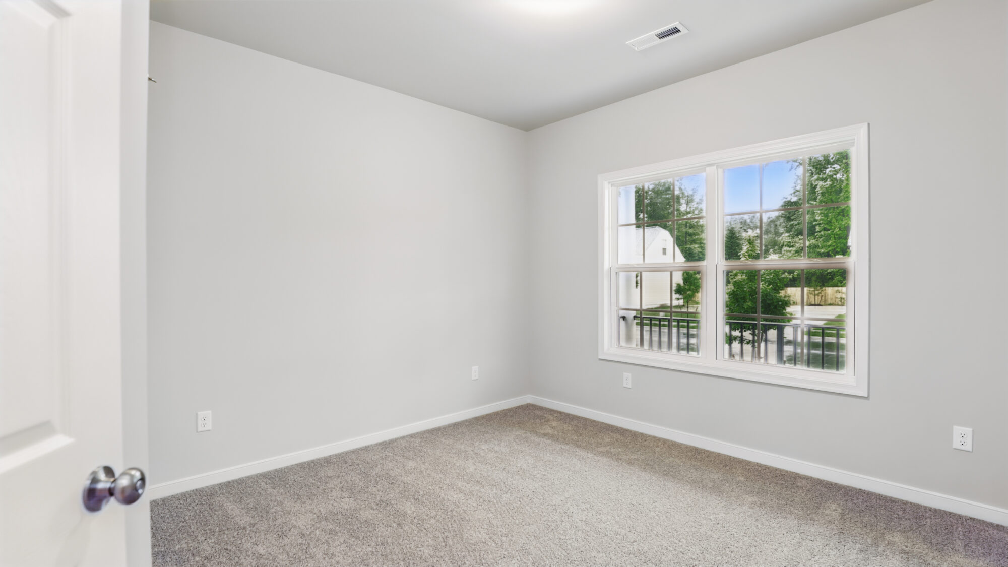 Empty carpeted room in Somerset Hill with light gray walls, white trim, and a window overlooking trees and driveway.