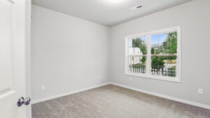 Empty carpeted room in Somerset Hill with light gray walls, white trim, and a window overlooking trees and driveway.