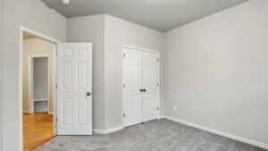 Empty room in Somerset Hill with light gray walls, gray carpet, double closet, and open door to hallway.