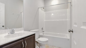 A modern bathroom at Somerset Hill with a white bathtub, toilet, and dark wood vanity with a marble countertop.