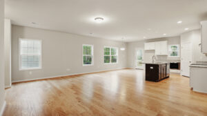 Spacious empty living area with hardwood floors in Bethany, featuring an open kitchen and white cabinets at Somerset Hill.