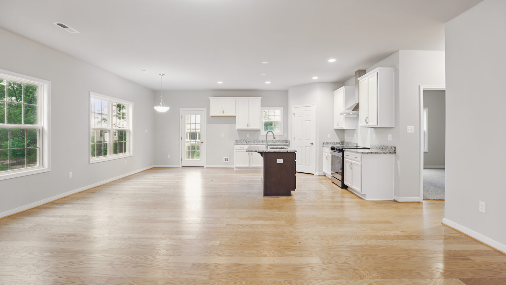 Bright, empty open kitchen and living area in Somerset Hill with hardwood floors, white cabinets, and large windows.