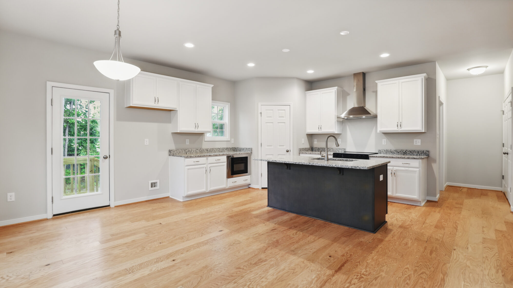 Modern kitchen at Somerset Hill with white cabinets, granite countertops, central island, and wooden floors.